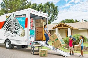 Photo shows 3 people unloading boxes from a U-Haul truck.